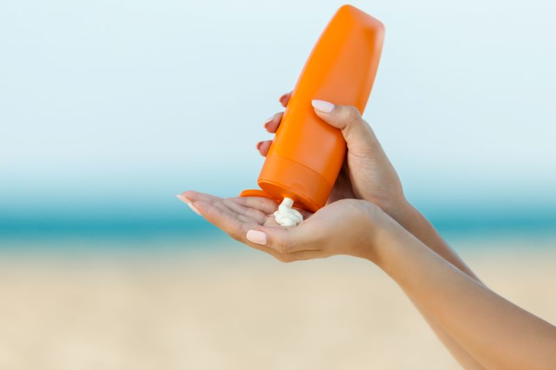 Une main appliquant un écran solaire sur la plage