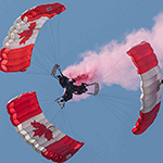 Trois côte-à-côte – Les trois SkyHawks sont maintenus ensemble par le parachutiste du milieu qui fait une clé de jambes aux deux parachutistes extérieurs. Seule la force musculaire brute permet de maintenir cette formation ensemble!