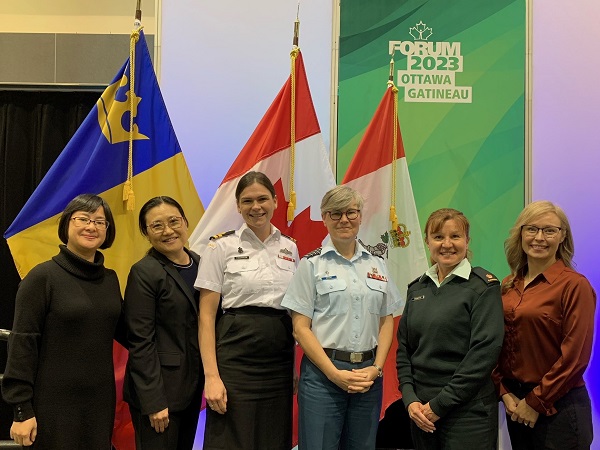 Six women, three of which are in uniform, pose in front of the Canadian and Royal Military College Flags while representing the Directorate of Women’s & Diversity Health at the 2023 Canadian Institute for Military and Veteran Health Research Forum in Gatineau, Quebec.