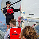 Four members of the 2023 RMC Varsity Club Sailing Team in action using a spinnaker during a practice (from L to R): OCdt Spencer Talerico (spinnaker sheets in hands, red hat), NCdt Mikhael Zavala Thyer (bowman, in charge of the spinnaker pole), NCdt Justin Norman (in the companionway), and OCdt Willem Quist (sitting in the cockpit).