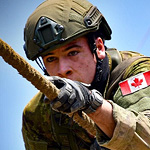 OCdt Josh Tremblay pulls himself across a rope while suspended 4.5 metres in the air. This obstacle is part of a larger approximately 1 km long obstacle course, which puts the participants through over 100 metres of elevation while sprinting, jumping, crawling, and climbing.