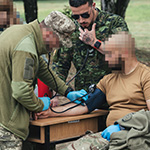 Un membre des Forces armées canadiennes (au centre) observe un membre des Forces armées ukrainiennes alors qu’il complète son évaluation finale pendant l’instruction médicale de combat tenu à l’élément d’instruction médicale, dans le cadre de l’opération UNIFIER, en Pologne, le 4 juin 2024. Photo prise par le matelot-chef Zach Barr, Forces armées canadiennes