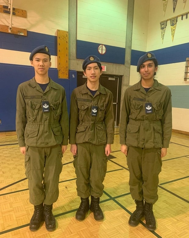 Trois caporaux cadets vêtus de l'uniforme d’entraînement en campagne se tiennent au garde-à-vous côte à côte.