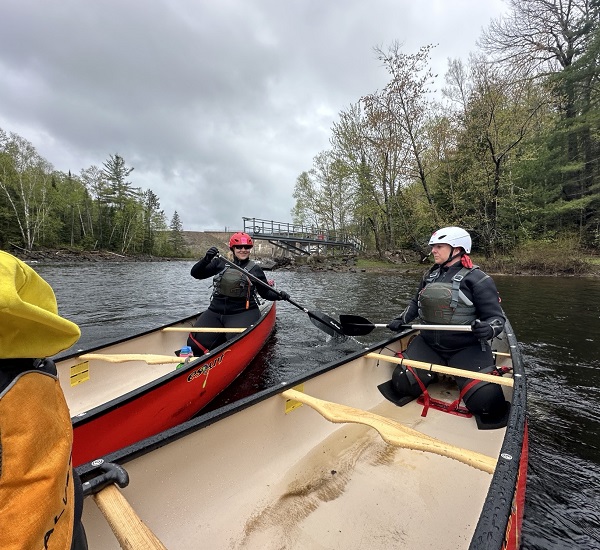 Participants paddle red canoes under an overcast sky during the True Patriot Love Madawaska Training Camp.