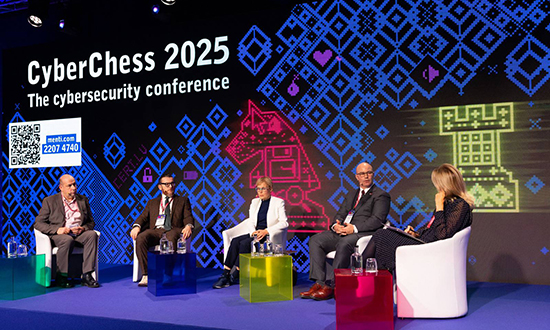 Brigadier-General Scott MacGregor responds to a question while seated on stage with four other panelists during CyberChess 2025 in Riga, Latvia, against a digital chess-themed backdrop.