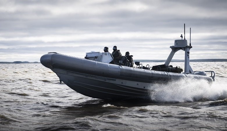 A small grey boat with three members of CANSOFCOM on board is moving at high speed under a cloudy sky.