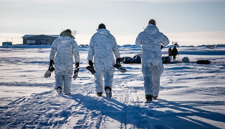 Three members of CANSOFCOM are walking towards equipment loaded up on toboggans. The landscape is flat and covered with snow.