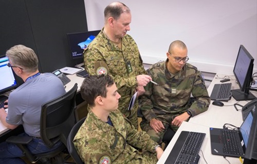 Canadian and French military cyber personnel review information on desktop screens during a NATO cyber exercise.