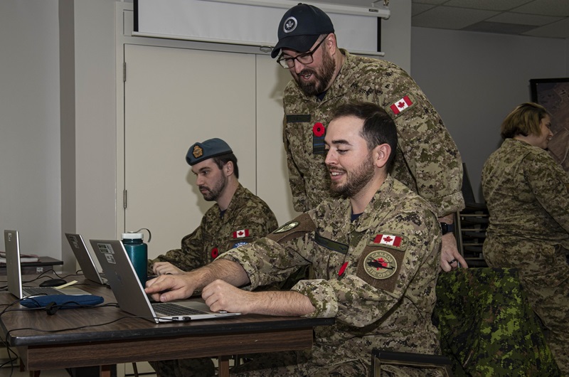 People in military uniforms working on computers at a table.