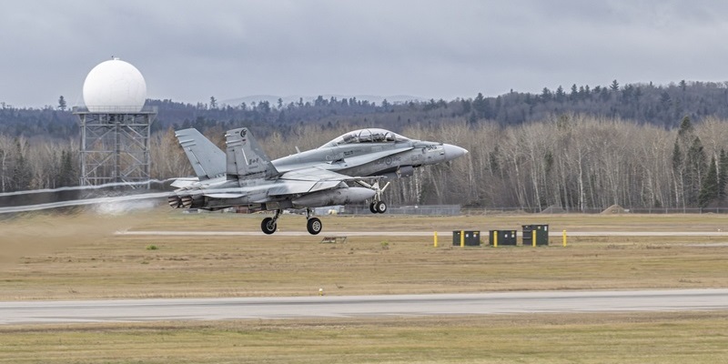 A jet aircraft taking off from a runway with trees in the background.
