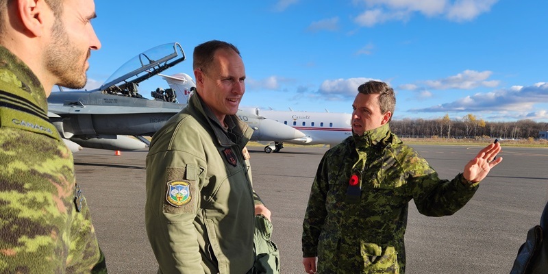 People in military uniforms talking outside with aircraft behind them.