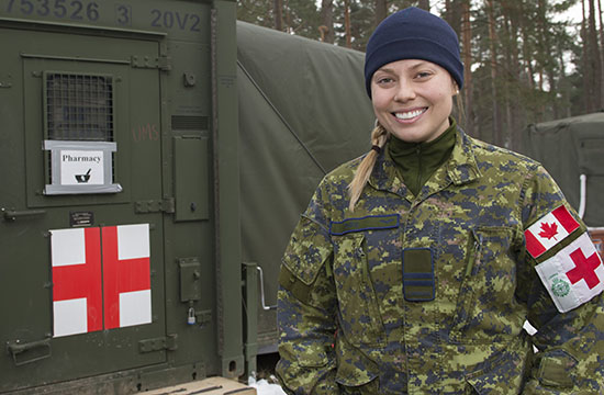 Canadian Armed Forces Pharmacy Officer stands near a field pharmacy marked with red cross and signs.