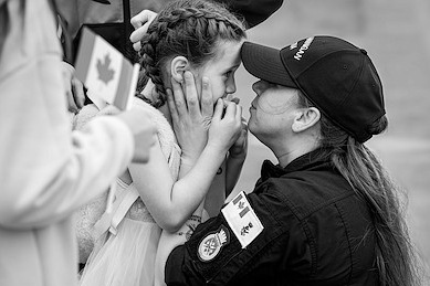 Her Watch Begins: A military parent kneels and kisses a young child, sharing a quiet emotional moment before departure.