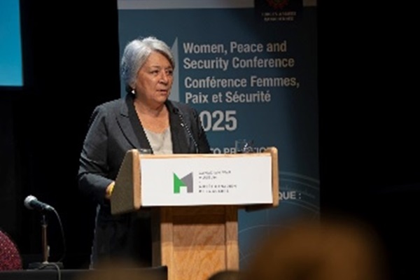 Une femme, Son Excellence la très honorable Mary Simon, est debout derrière un podium d’où elle s’adresse aux participants de la conférence.