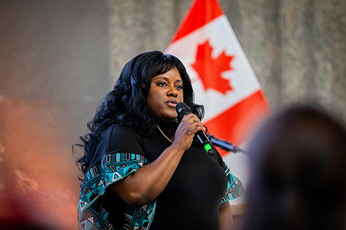 Woman singing into a microphone with a Canadian flag in the background.