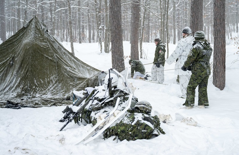 CAF members and UK military nurse assemble a tent in a snowy forest during training.