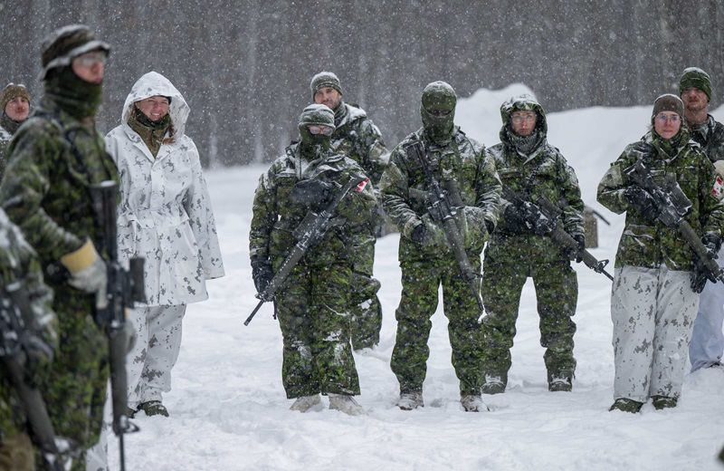 Group of CAF members and UK military nurse standing in snowy conditions receiving training instructions.