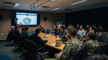 Royal Canadian Navy personnel deliver a briefing to Canadian Armed Forces and Five Eyes participants gathered around a conference table during the Cyber Mission Assurance tabletop exercise.