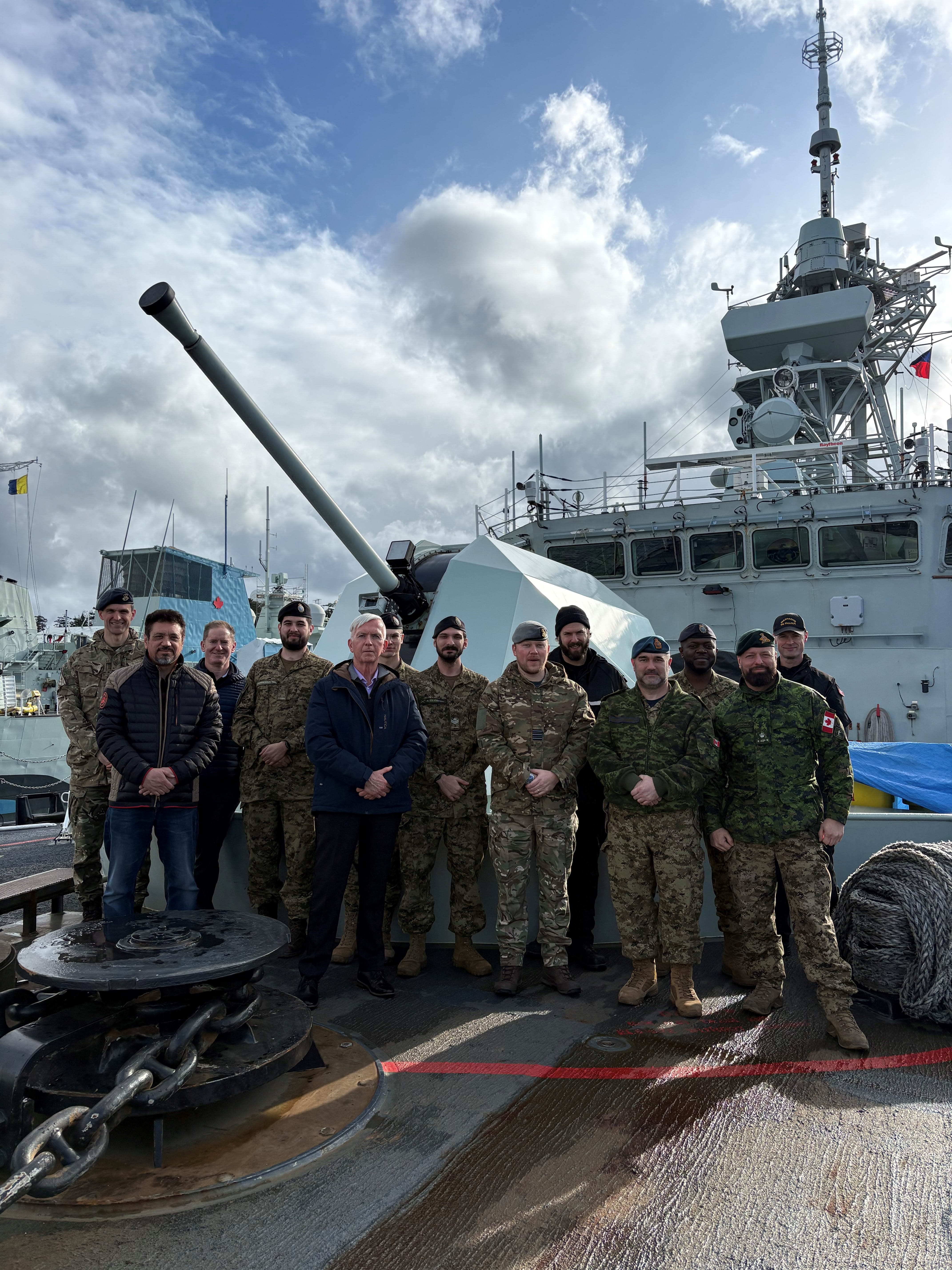 CAF and Five Eyes tabletop exercise participants stand on the deck of HMCS Regina beside the ship’s main gun during a familiarization visit in Esquimalt, British Columbia.