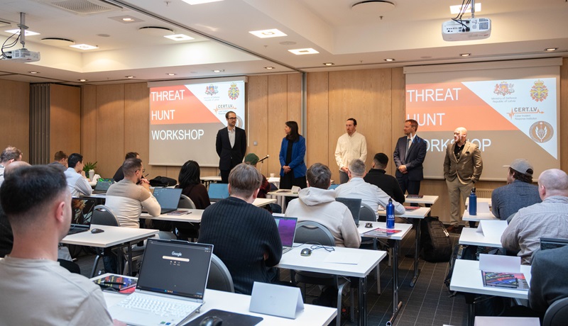 A classroom of international participants using laptops while instructors present at a cybersecurity threat hunting workshop.