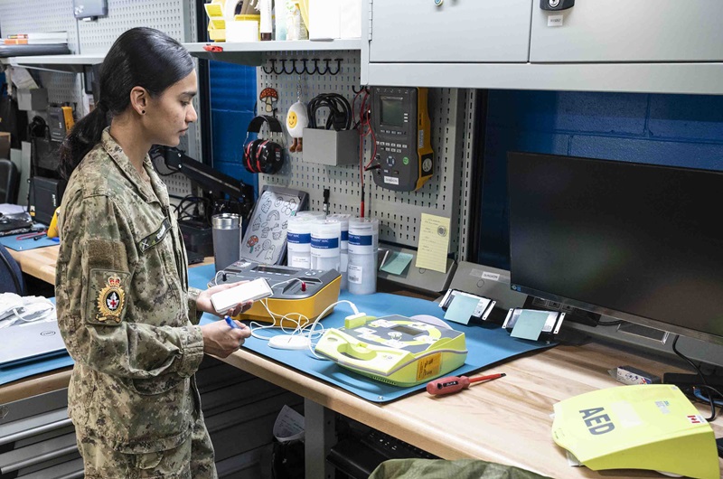 CAF technician inspects an AED+ on a workbench using biomedical test equipment.