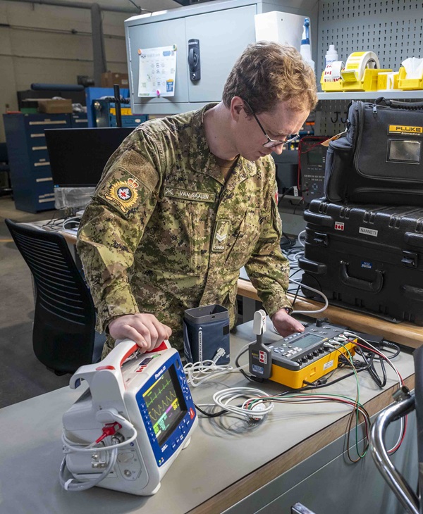 CAF technician tests a patient monitor with cables and an analyzer on a laboratory bench.