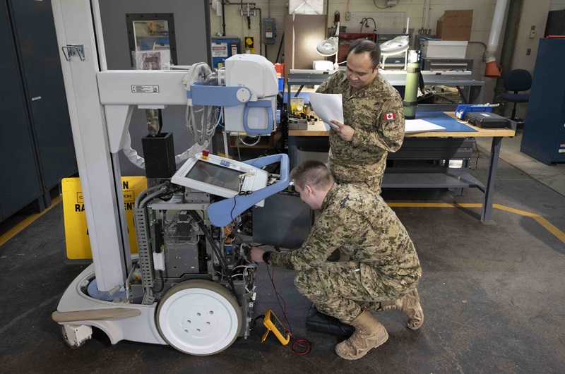 Two CAF technicians inspect a mobile X-ray unit with panels open in a maintenance bay.