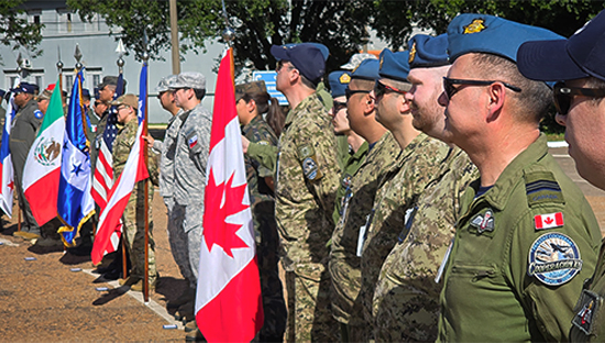 Military personnel from multiple countries standing in a line during a formal outdoor ceremony, featuring flags from Canada, the United States, and Mexico.