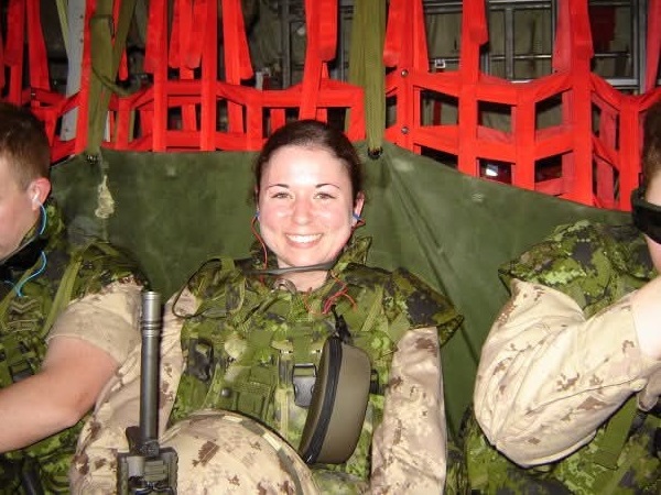 A soldier in uniform is sitting in an aircraft, smiling at the camera.