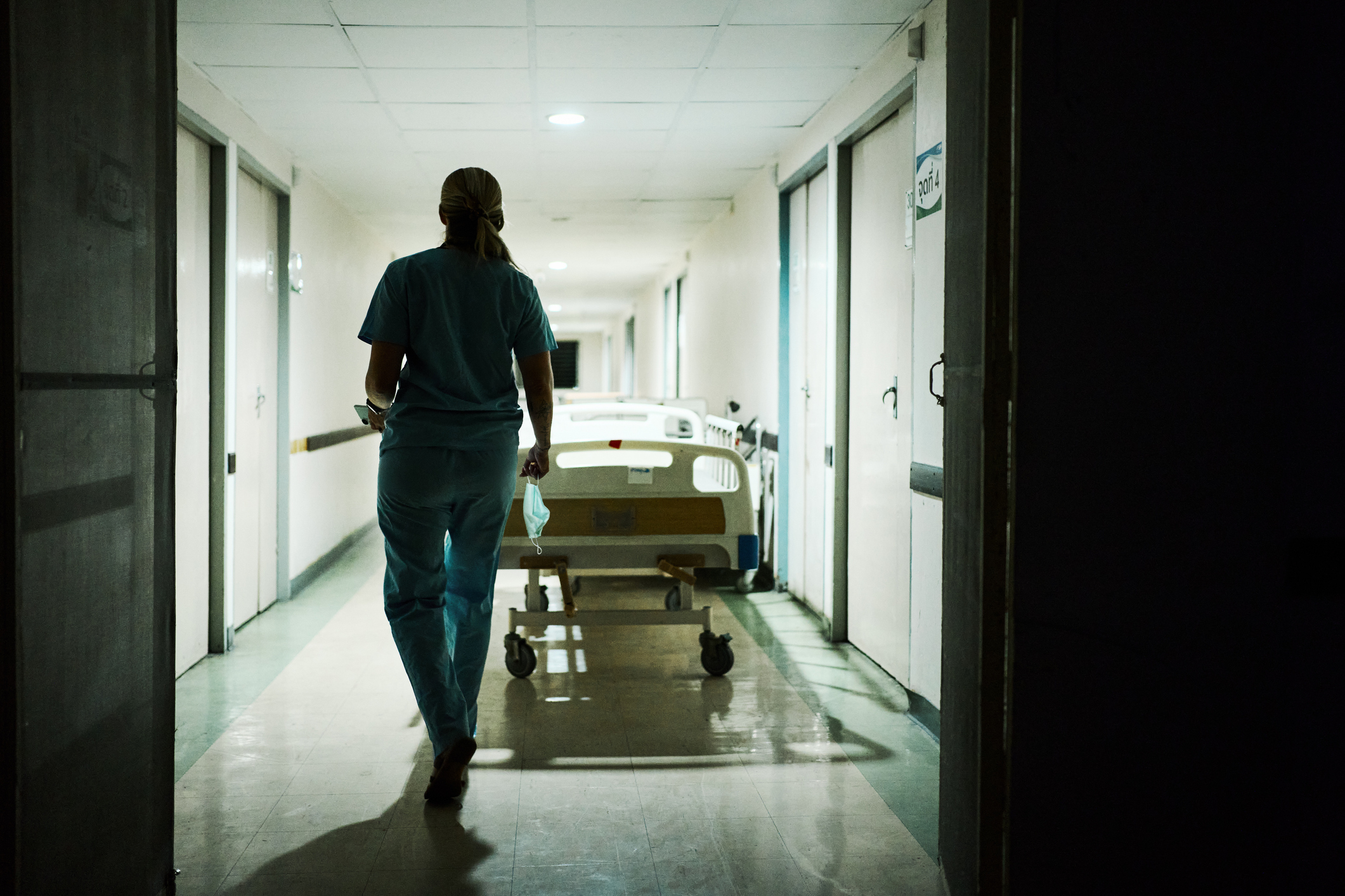 Full length rear view of medical professional in scrubs walking through hospital corridor during nighttime.