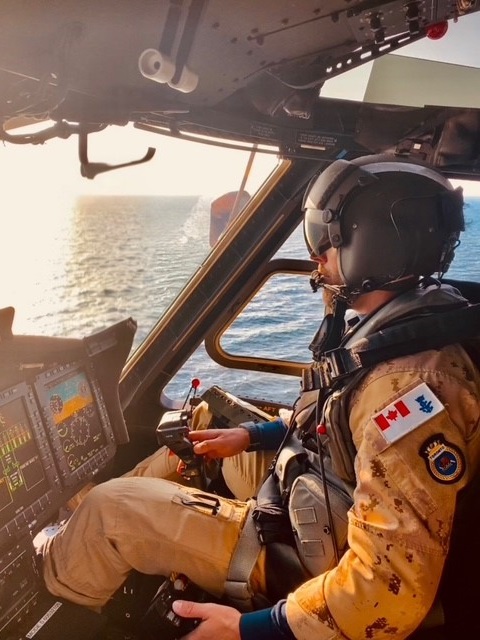 A soldier is flying a helicopter over the sea and looking over the horizon.