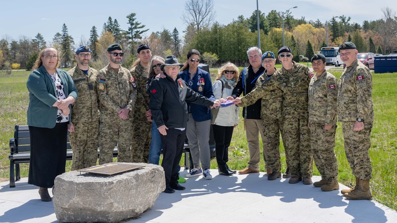 Group of individuals standing together at a commemorative monument outdoors, during a ceremonial event.