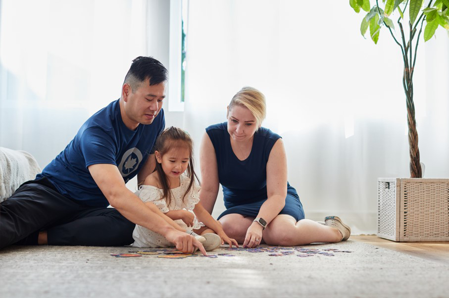 A father, child, and mother sitting down on the floor and playing a game together.