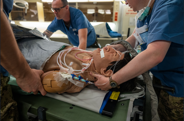 Medical staff perform simulated emergency care on intubated training mannequin on stretcher in clinical lab.