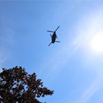 A CH-147 Chinook helicopter passes overhead against a clear sky during the 25th anniversary commemoration at the National Military Cemetery.