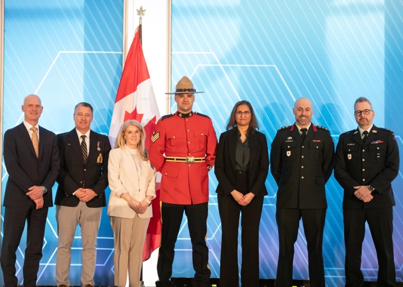 Seven award recipients and presenters stand in a row on a stage in front of a large Canadian flag and a blue backdrop. The group includes individuals in business attire, an RCMP red serge uniform, and military uniforms. The photo was taken during the presentation of the Excellence in Data and Information Stewardship Award at the 2026 Digital Government Community Awards Gala in Ottawa.