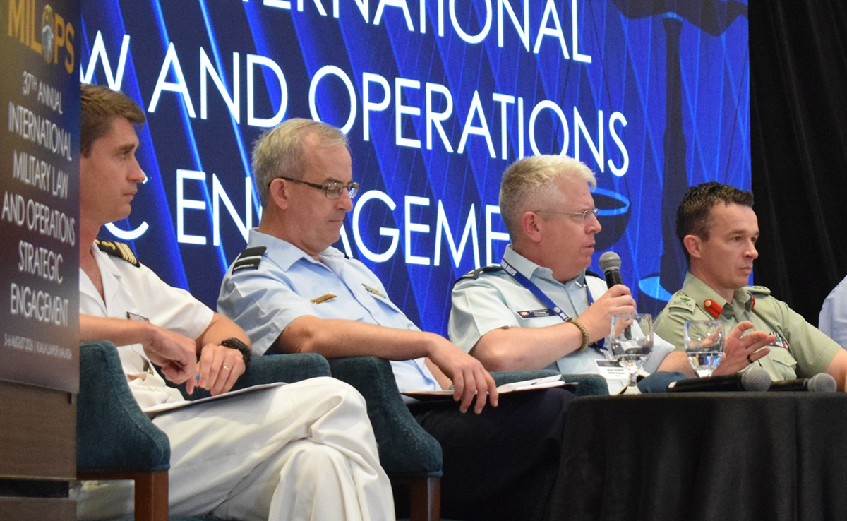 Major-General Robin Holman speaks into a microphone alongside fellow panellists at MILOPS 2026.