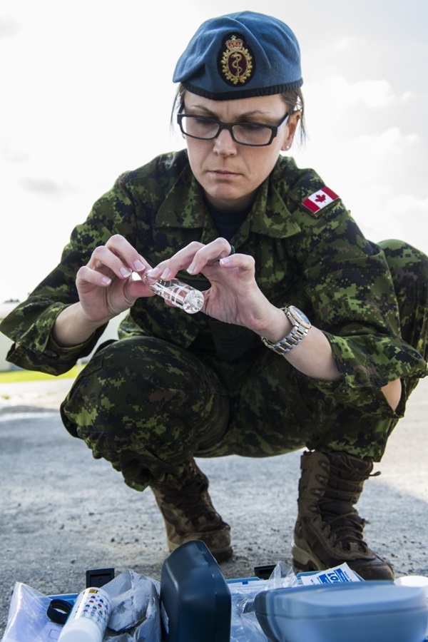 CAF member crouches beside testing equipment, examining a sample vial during field water analysis.