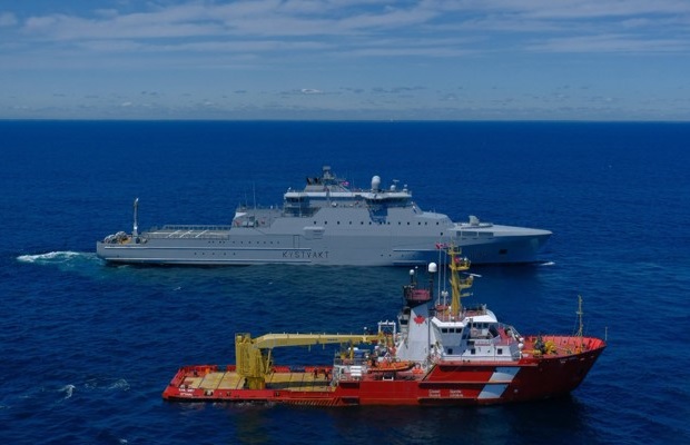 A large red ship and a large grey ship sail side by side on the blue ocean.