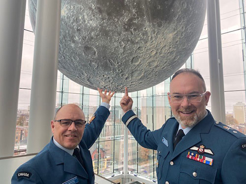 Two uniformed individuals reach towards a model of the moon.