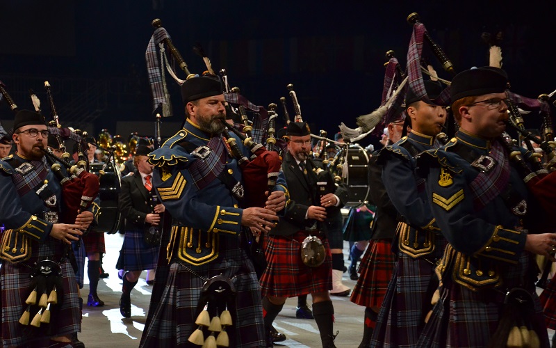 Royal Canadian Air Force Pipes and Drums members (left to right) Captain Dylan Podkowka, Sergeant Bill MacDougall and Corporal Hayden Landolt march while playing the bagpipes with the massed pipes and drums at the Norfolk Scope Arena during the Virginia International Tattoo in Norfolk, Virginia on 23 April 2025. Many pipers and drummers from other countries are seen in the background, marching in the same formation.