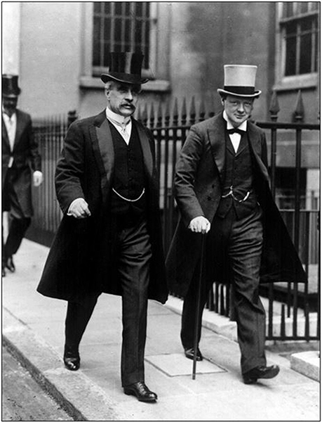 Two men dressed in suits and top hats walk on the sidewalk.