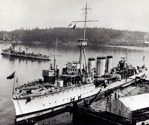 An overhead view of a docked ship. Another ship leaves the docks in the background.