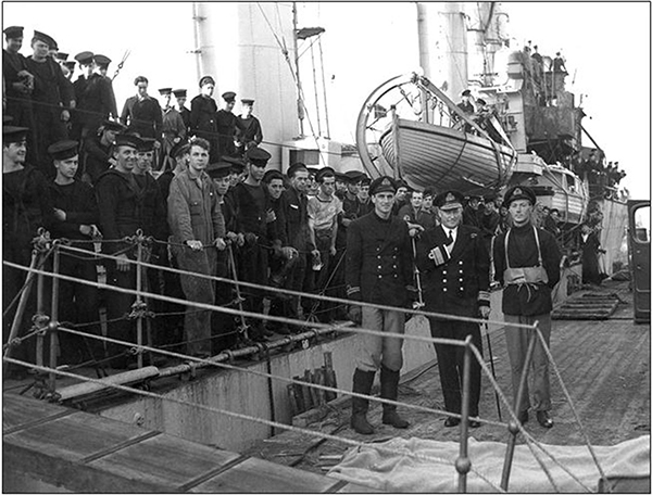 Naval personnel pose for a picture on a ship tied to a dock.