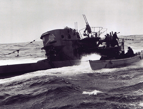 A small boat tied to a surfaced submarine which bobs on the water.