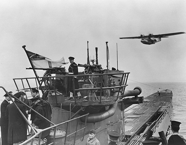Men discussing on the ship as a plane flies overhead.