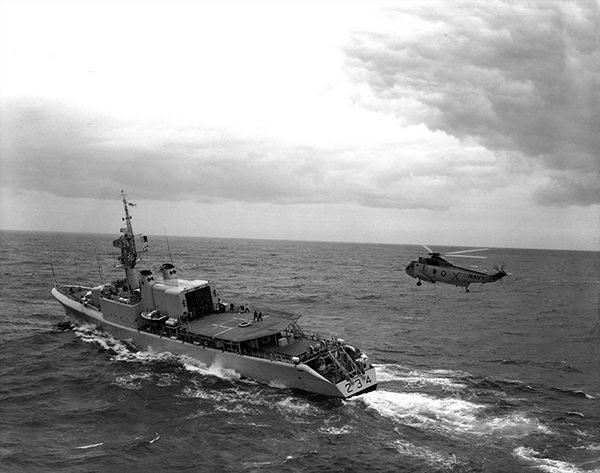 A helicopter lands on a ship travelling through the water.