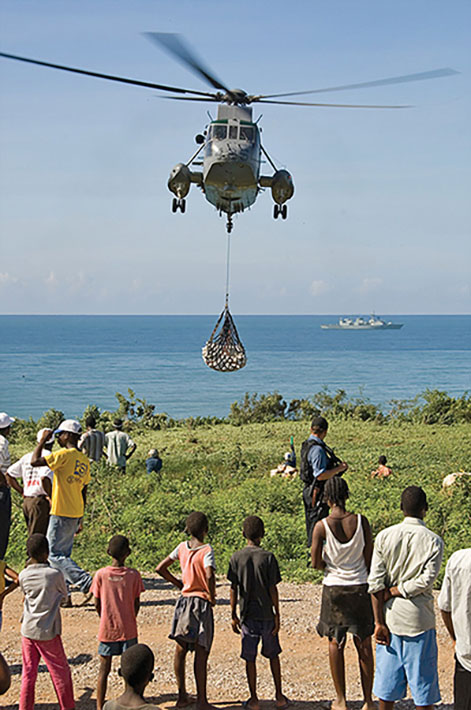 A helicopter delivers relief goods to a crowd of people.