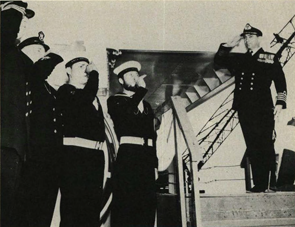 The captain standing on the stairs of the ship and a row of sailors piping.