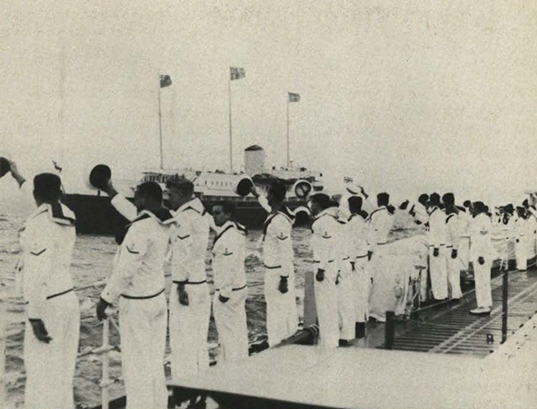 Soldiers on the side of the deck of a ship saluting another ship.
